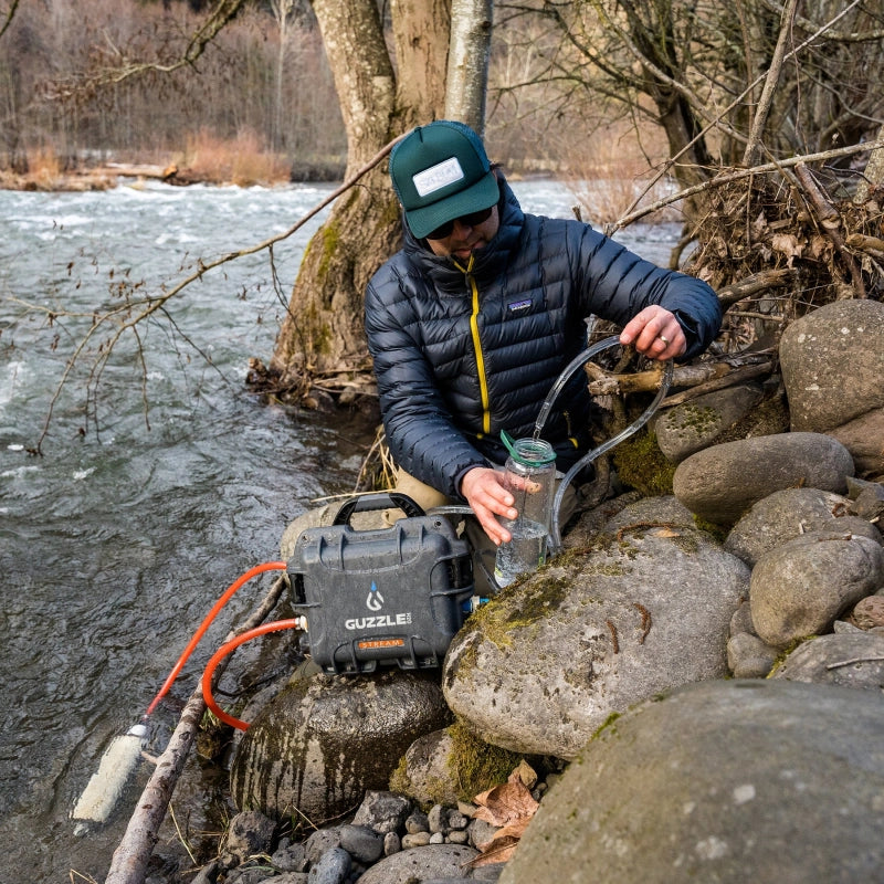Guzzle H2O Guide Prefilter connected to a Stream portable water purification system beside a river during backcountry water collection.